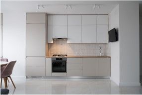 Modern minimalist kitchen with light gray cabinets, light wood countertop, and small black TV on the wall.