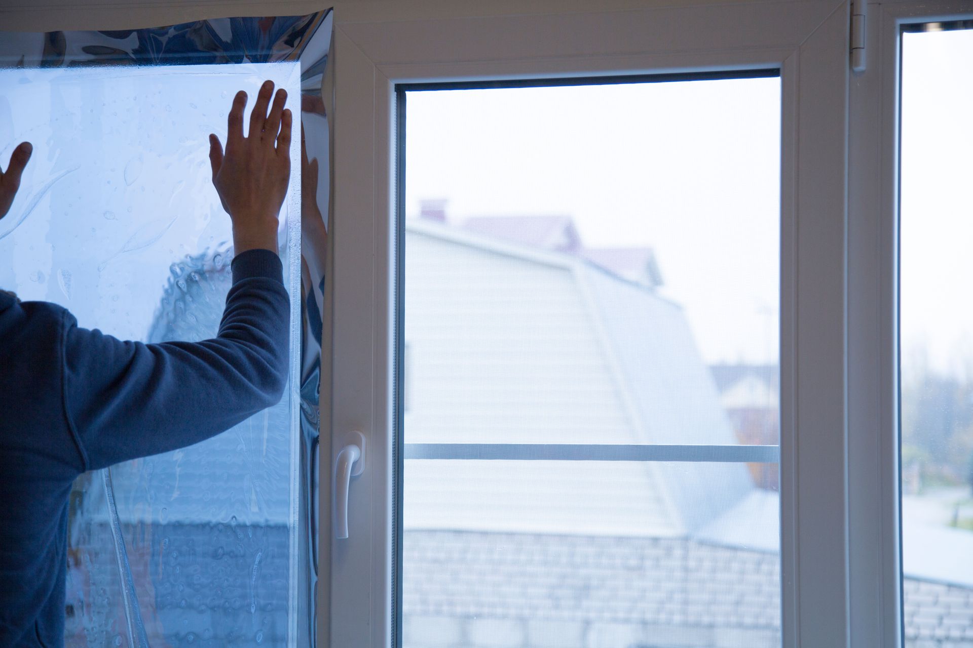 Person applying protective window film to a large glass door, smoothing the surface. Person applying protective window film to a large glass door, smoothing the surface.