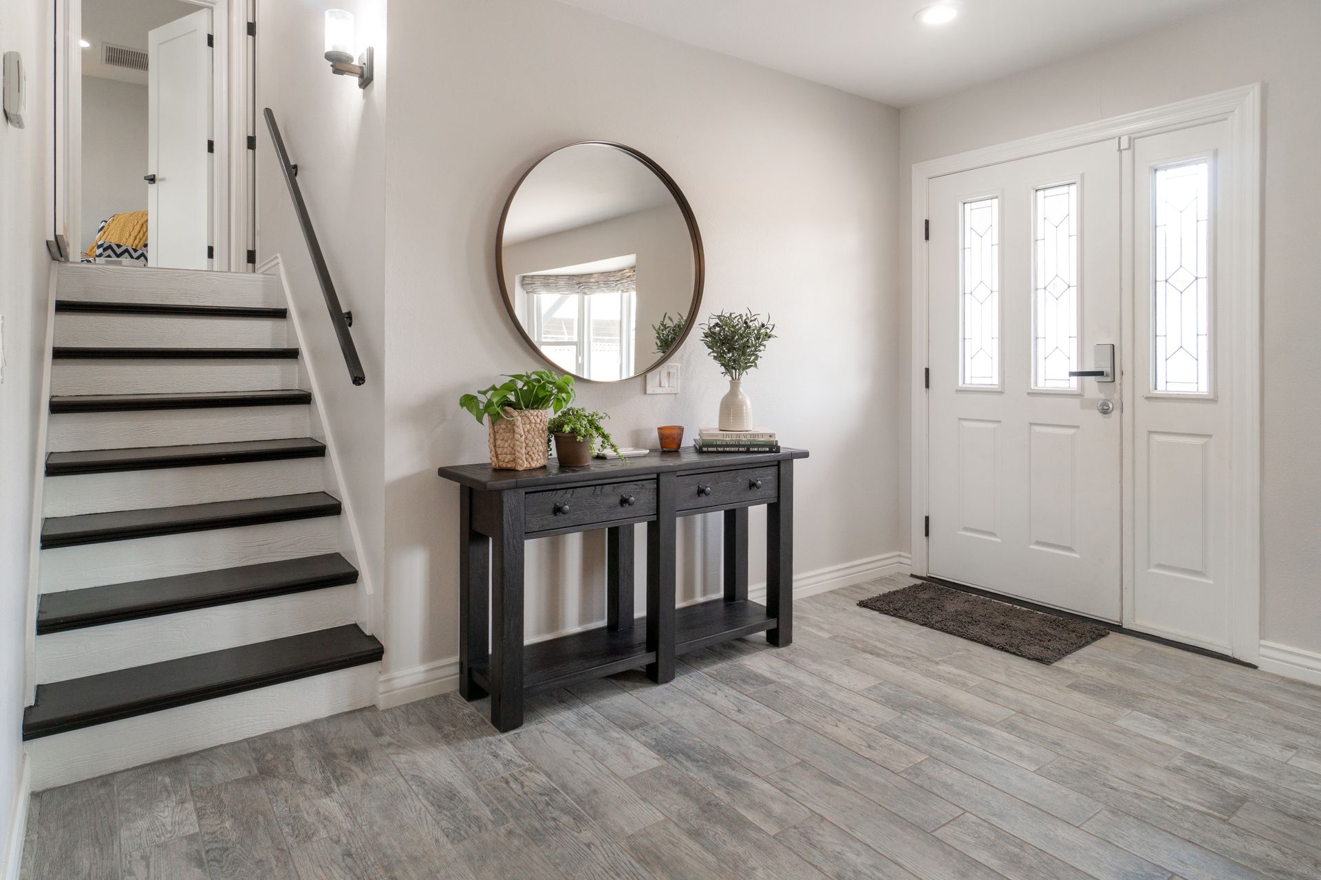 A stylish entryway featuring a round mirror, black console table, and staircase.