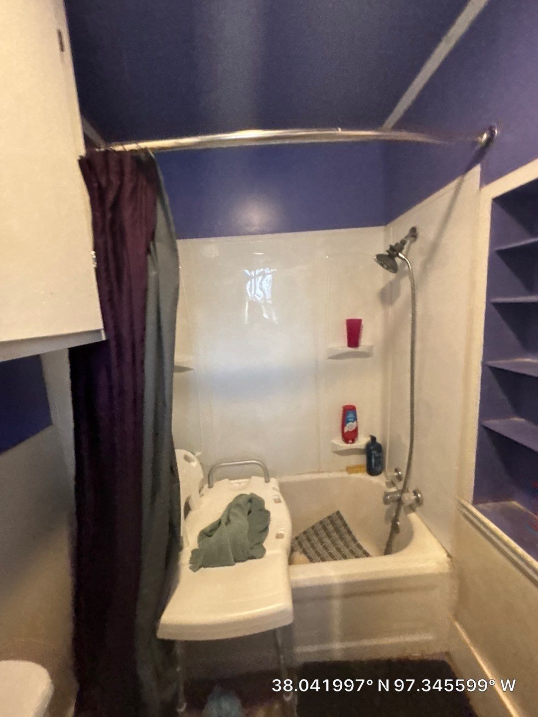 A small bathroom with purple walls, a white bathtub and shower