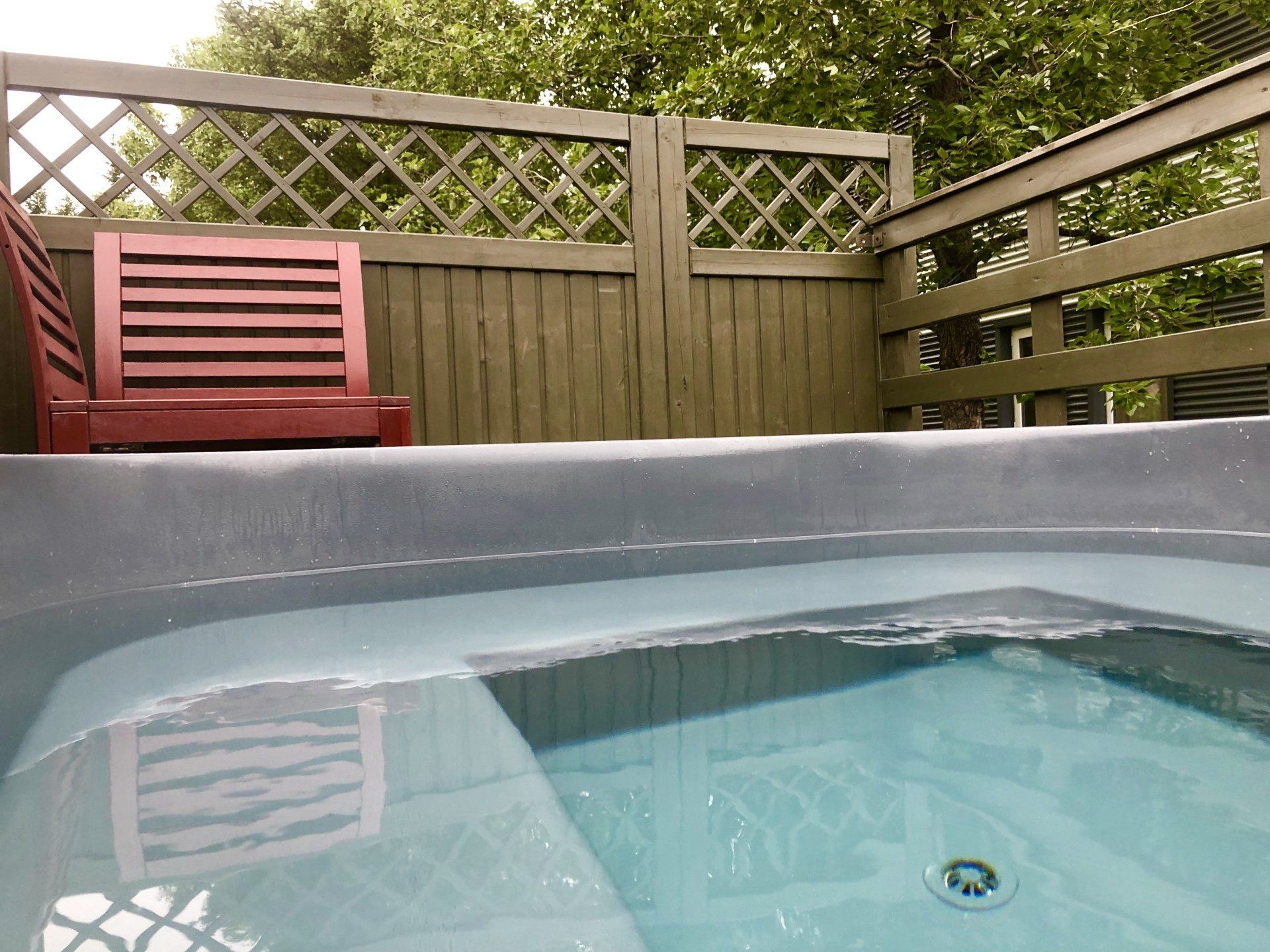 A hot tub with a chair in the background and a fence in the background.