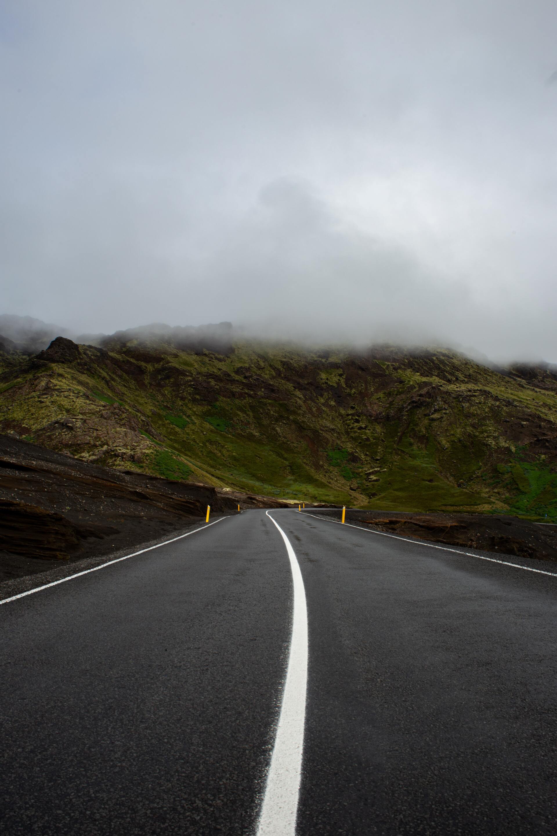 A road with a white line on it going through a foggy mountain.