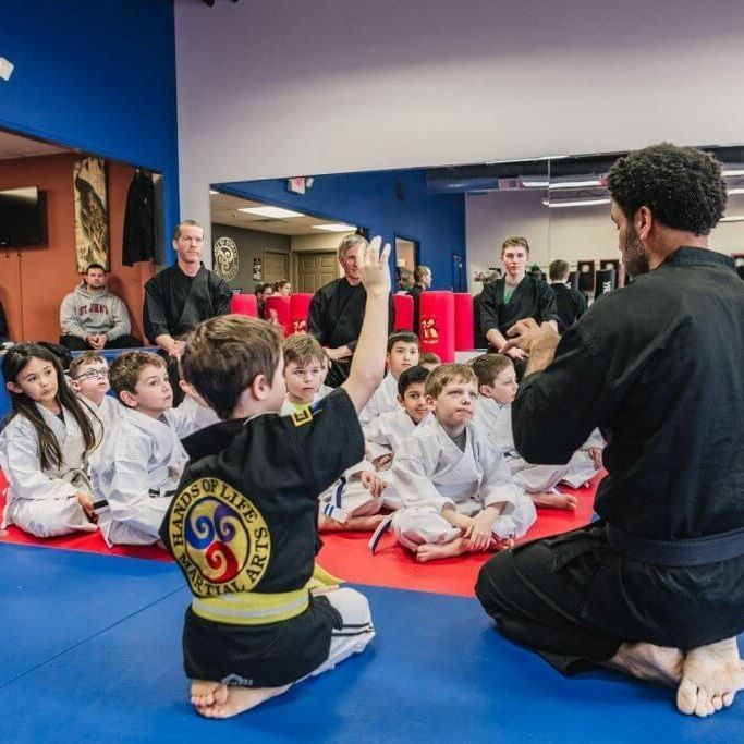 A group of kids are sitting on the floor in a martial arts class