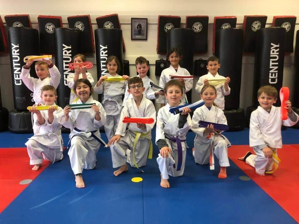 A group of young karate students are posing for a picture in a gym.