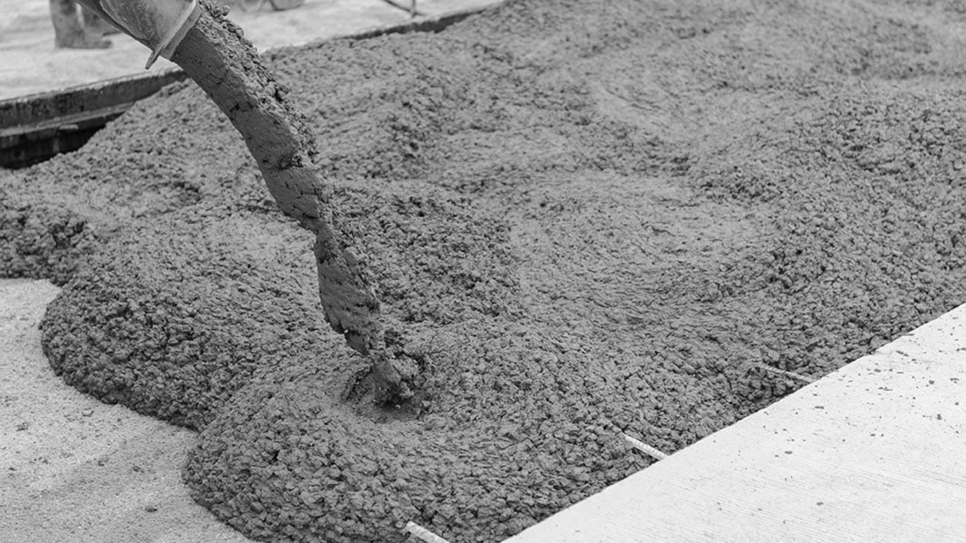 Concrete being poured from a pump hose onto a construction site surface.