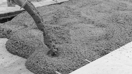 Concrete being poured from a pump hose onto a construction site surface.