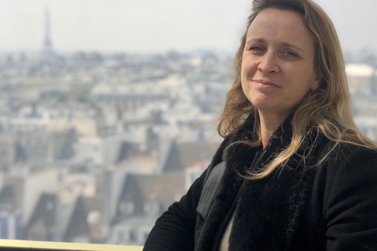 Une femme dans un manteau noir se tient devant l'horizon d'une ville.