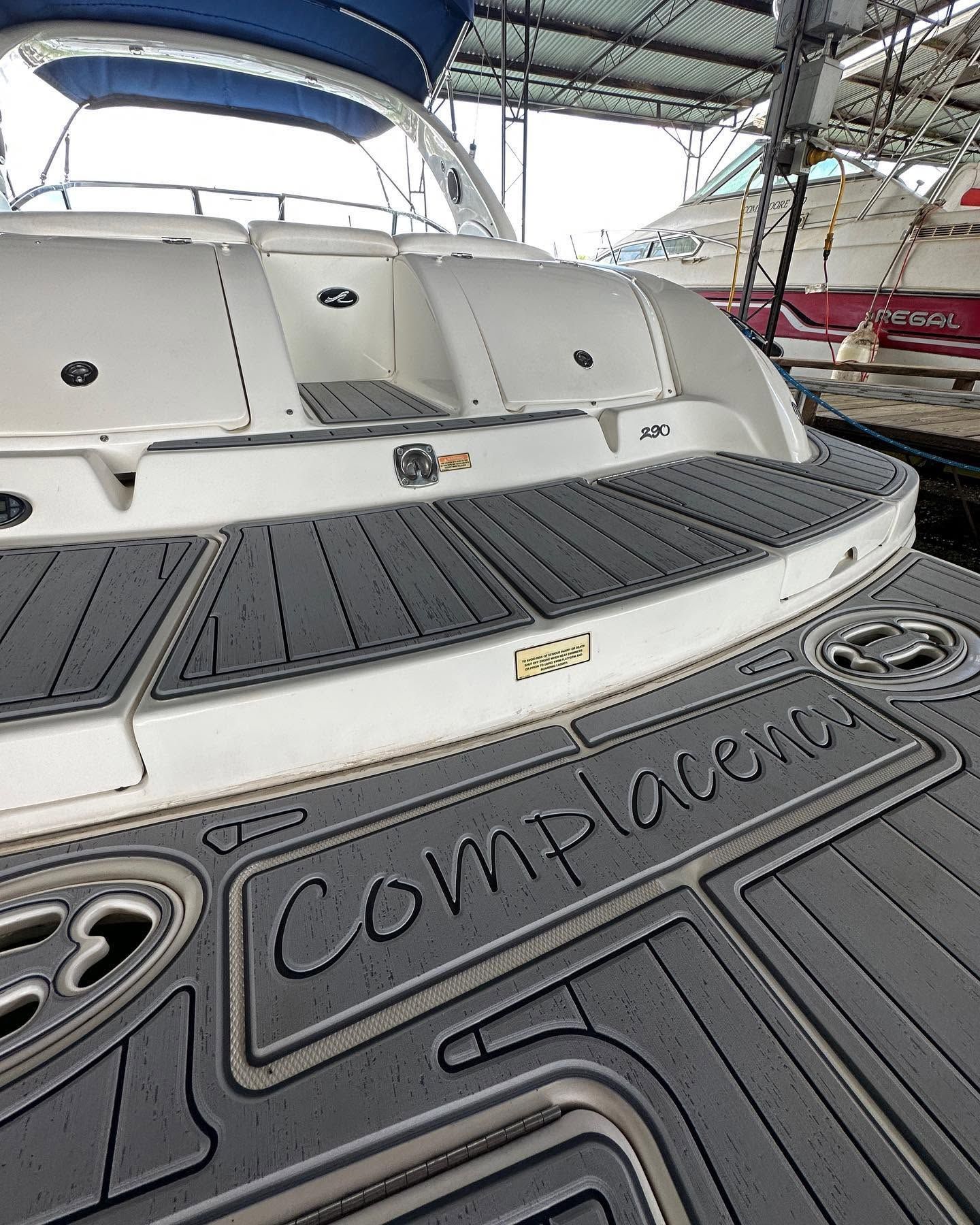 White yacht stern with gray deck in a covered marina, labeled “Complexa.”