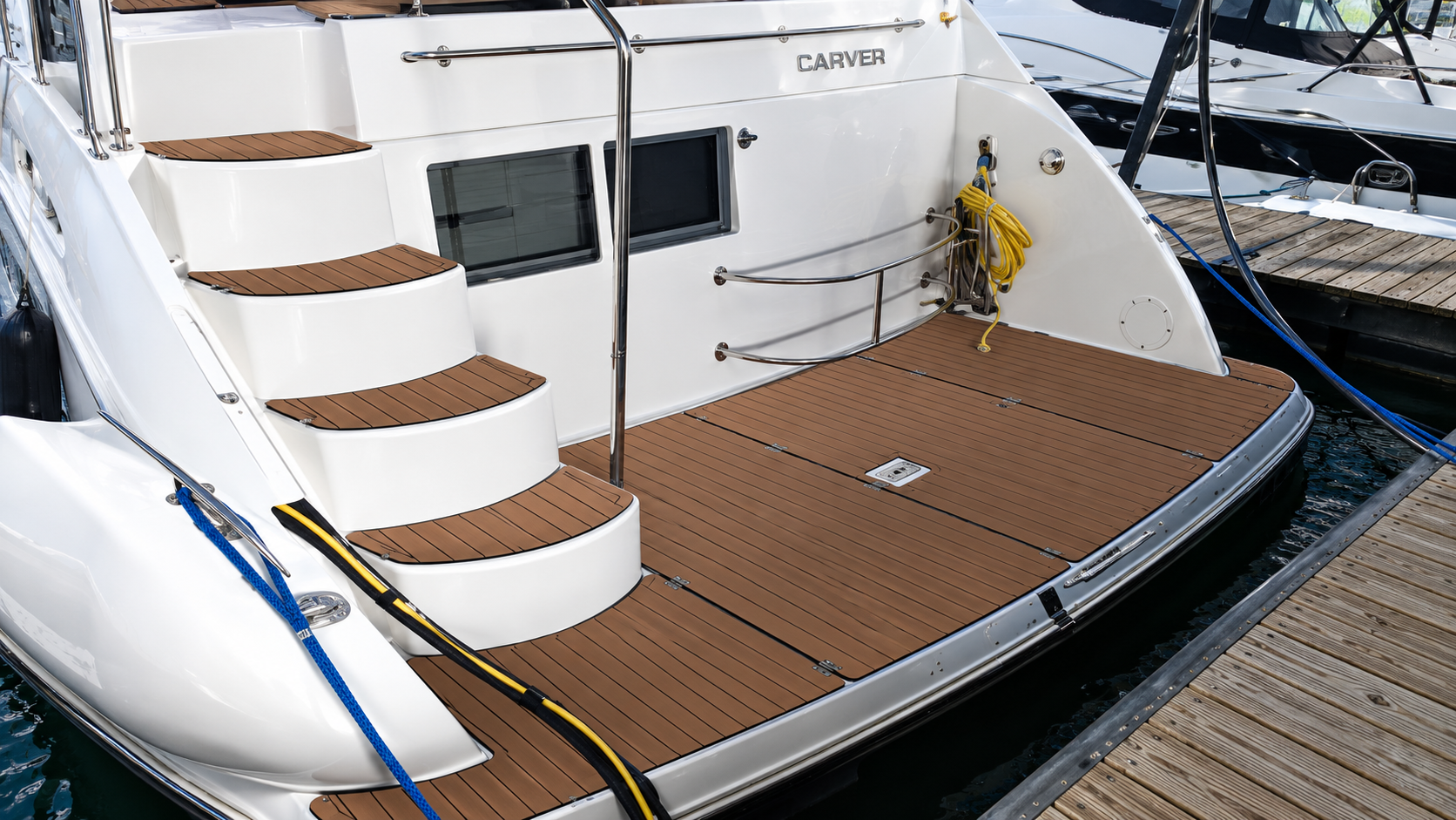 White yacht stern with teak deck and curved steps, docked beside a wooden pier.