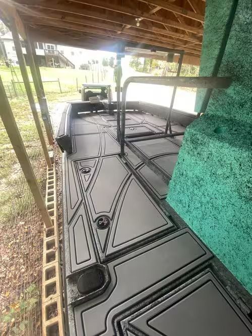 Black modular deck panels stored under a covered patio beside a green wall.