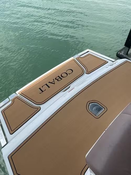 Boat deck with tan cushions and “COBALT” logo beside green water