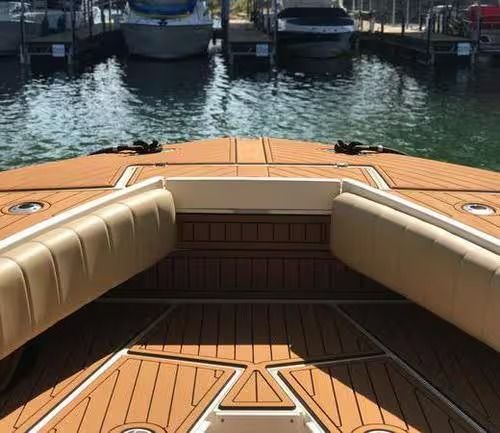 View from a boat deck with tan cushions and wooden flooring, facing calm marina water and docked boats.