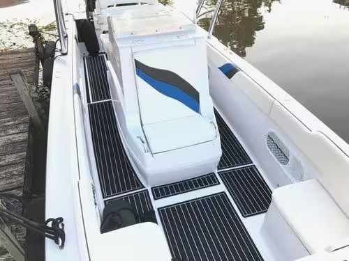 White boat deck with black-and-white non-slip flooring, blue-striped hatch, and calm water beside it