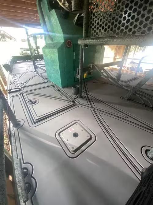 Gray metal deck with raised hatches and cables under green industrial equipment