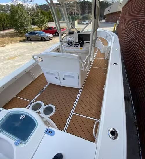 White center-console fishing boat with tan deck walkway, docked beside a brick building.