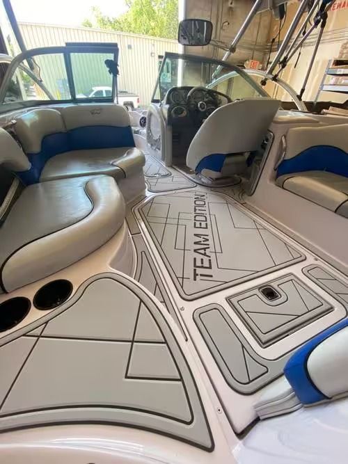 Boat cabin seating area with gray and blue cushioned benches and a central floor panel in a garage.