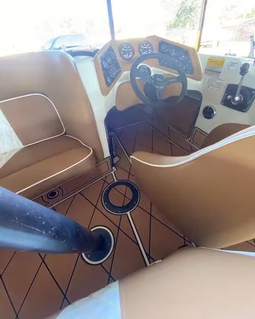 Boat cockpit with steering wheel, gauges, tan seats, and navy carpet flooring