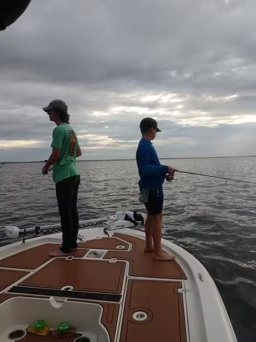 Two people fishing from the bow of a boat on a cloudy lake at dusk