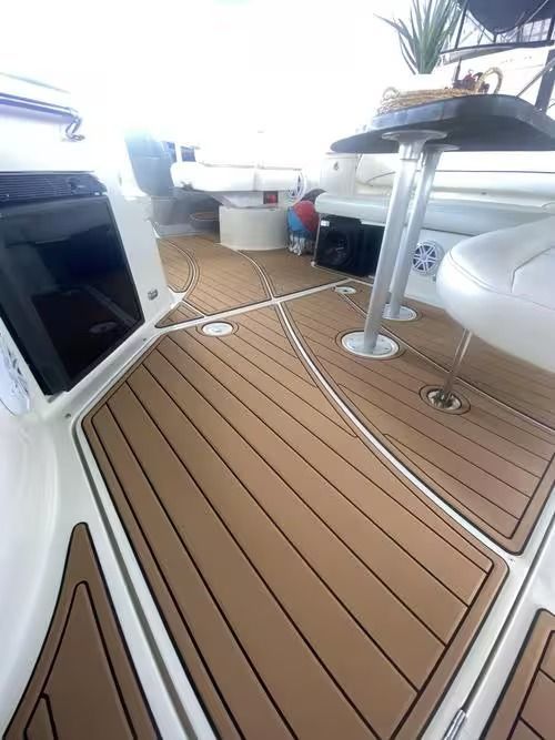 Boat deck with tan teak flooring, white seating, and glass-topped table in a bright cabin area
