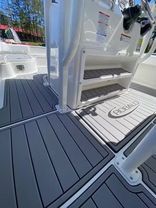 Boat deck with gray nonslip flooring and steps leading to a cabin entrance in bright sunlight