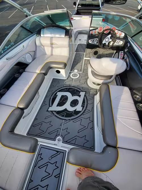 Boat cockpit with gray seating, steering wheel, and patterned deck mat with a “DD” logo