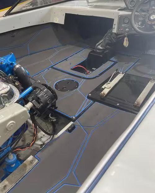 Boat interior with exposed engine, black floor hatch, and blue tape outlines on gray decking.