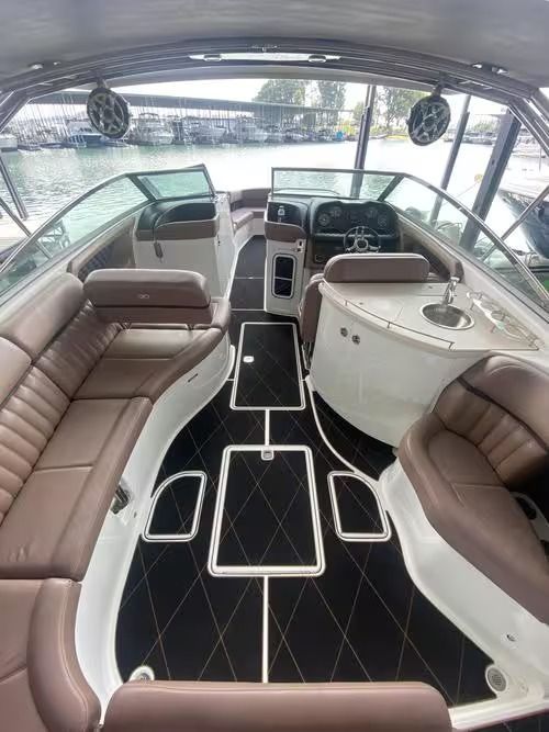 Boat cabin interior with tan leather seating, black carpet, and a helm view through the windshield