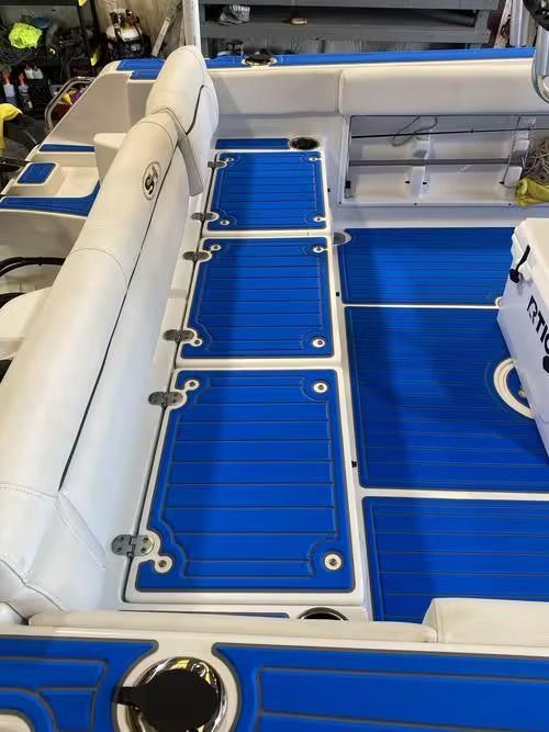 Blue deck floor with white padded seating and storage hatches on a boat interior