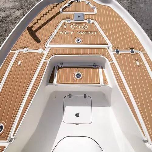 Top-down view of a boat deck with tan teak-style flooring, white hatches, and “Key West” lettering.