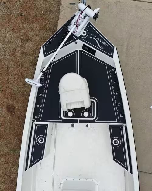 Top-down view of a black-and-white model boat on concrete, with a white seat and mounted equipment.
