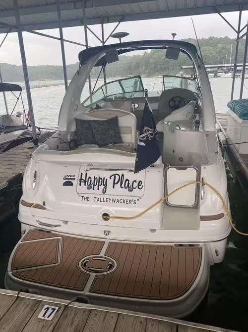 Stern of a white boat named Happy Place docked under a covered marina, with a wood-finish swim platform.