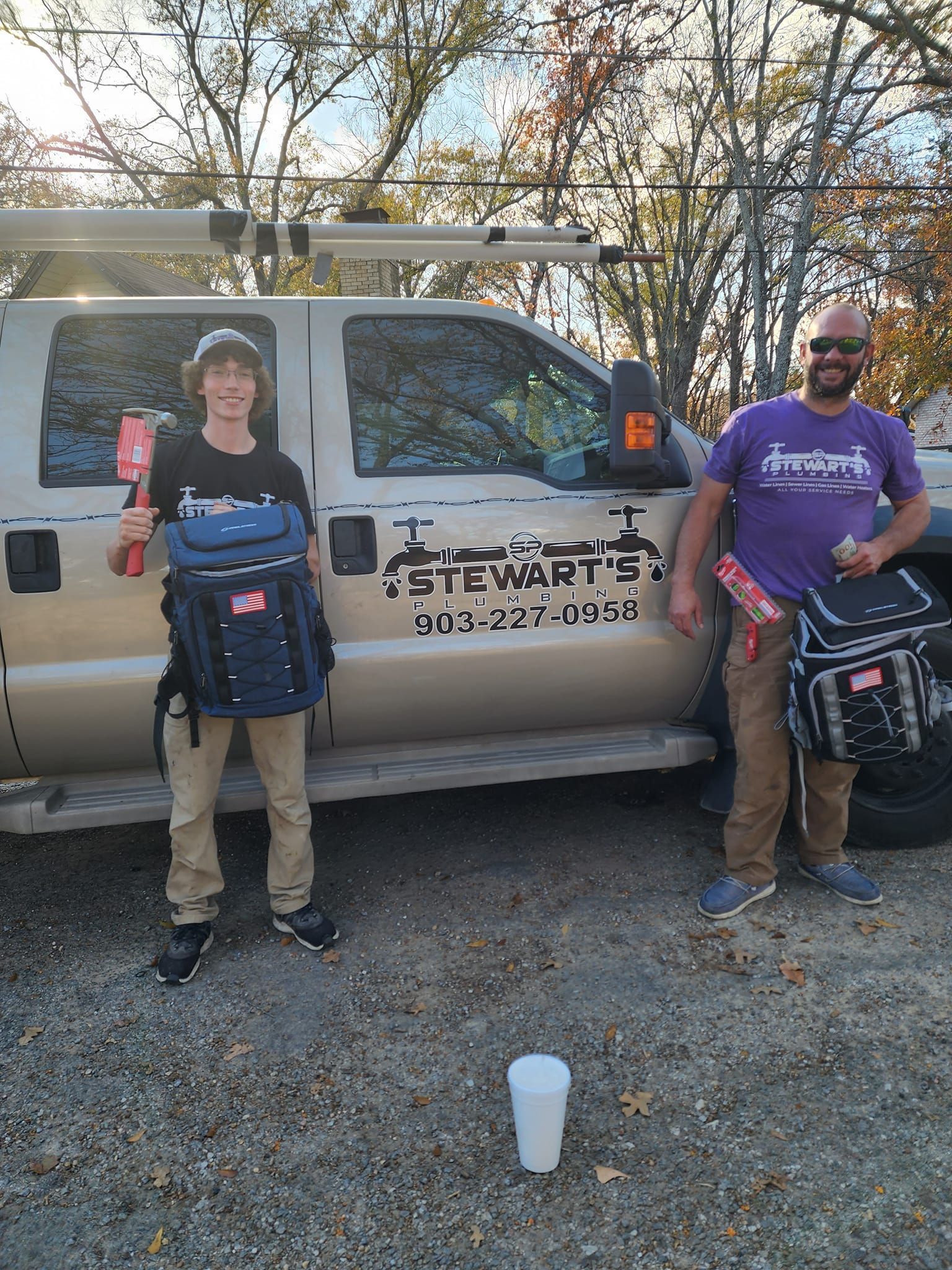 Two men stand by a truck with tool bags, holding items.