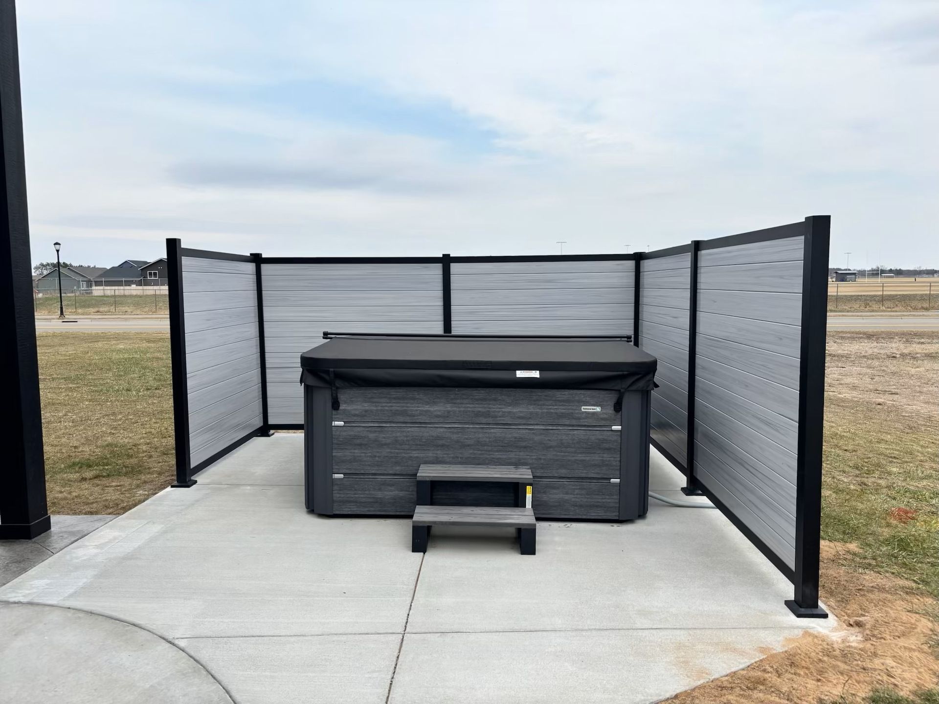 Outdoor hot tub on a concrete patio with gray privacy screens and open field background