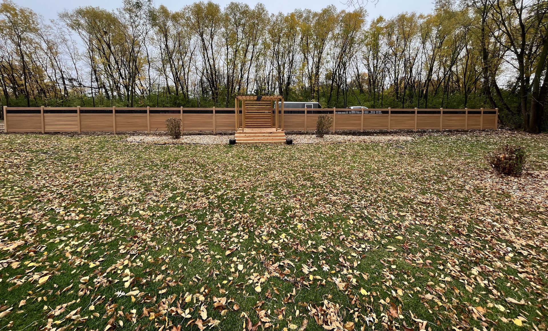 Outdoor wooden deck with benches in a flower-covered field, bordered by a fence and trees