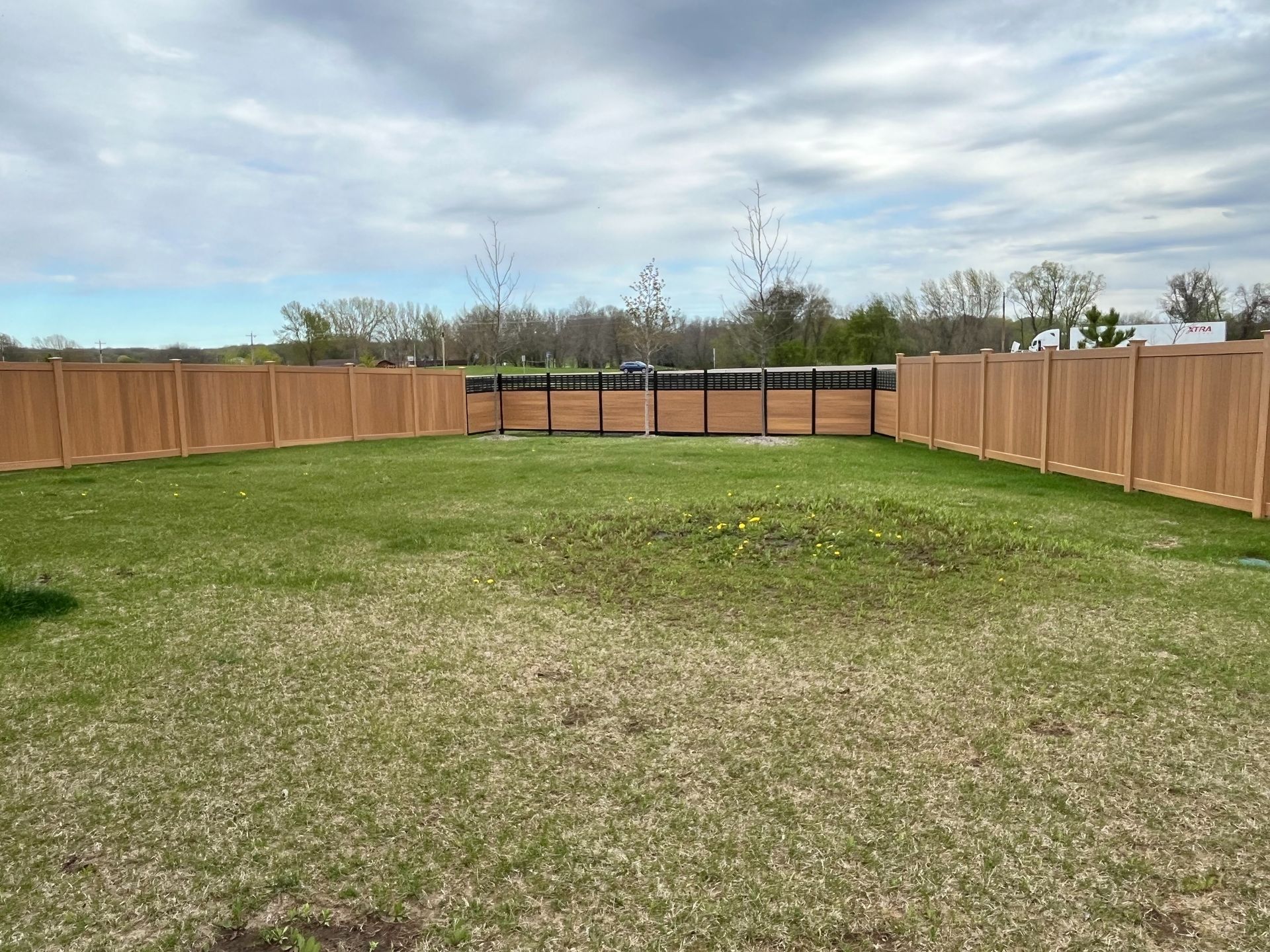Large fenced backyard with a grassy lawn and cloudy sky