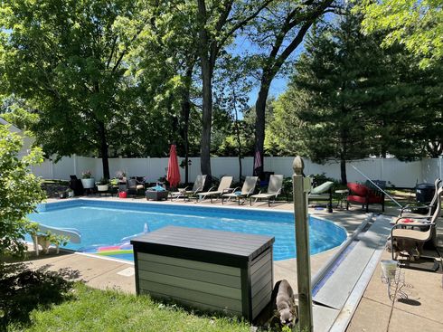 Backyard pool with lounge chairs, trees, and a gray storage box on the deck