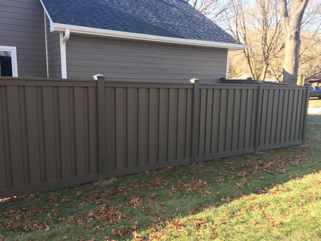 Brown privacy fence along a house and leaf-covered lawn in a backyard