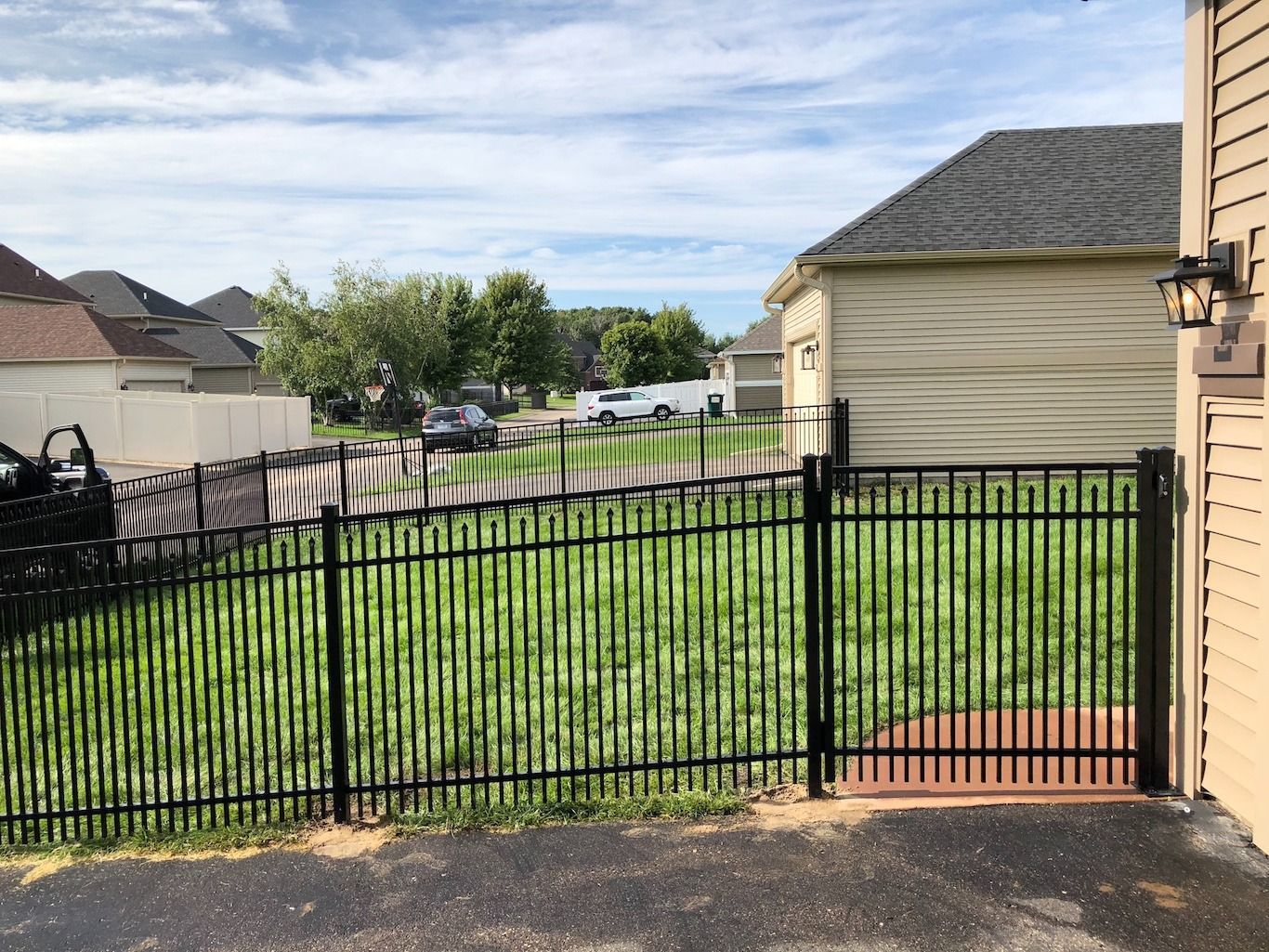 Black metal fence beside a beige house, with a green lawn and neighboring homes in the background.