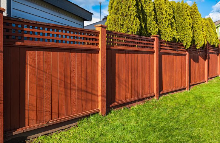Wooden privacy fence with red-brown panels along a green lawn beside a house