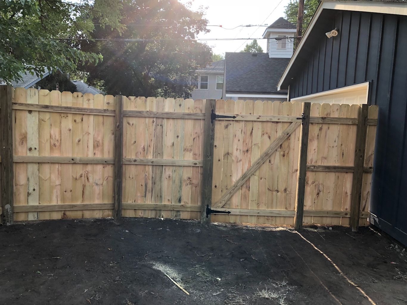 Freshly built wooden fence with a gate in a small backyard beside a dark house.