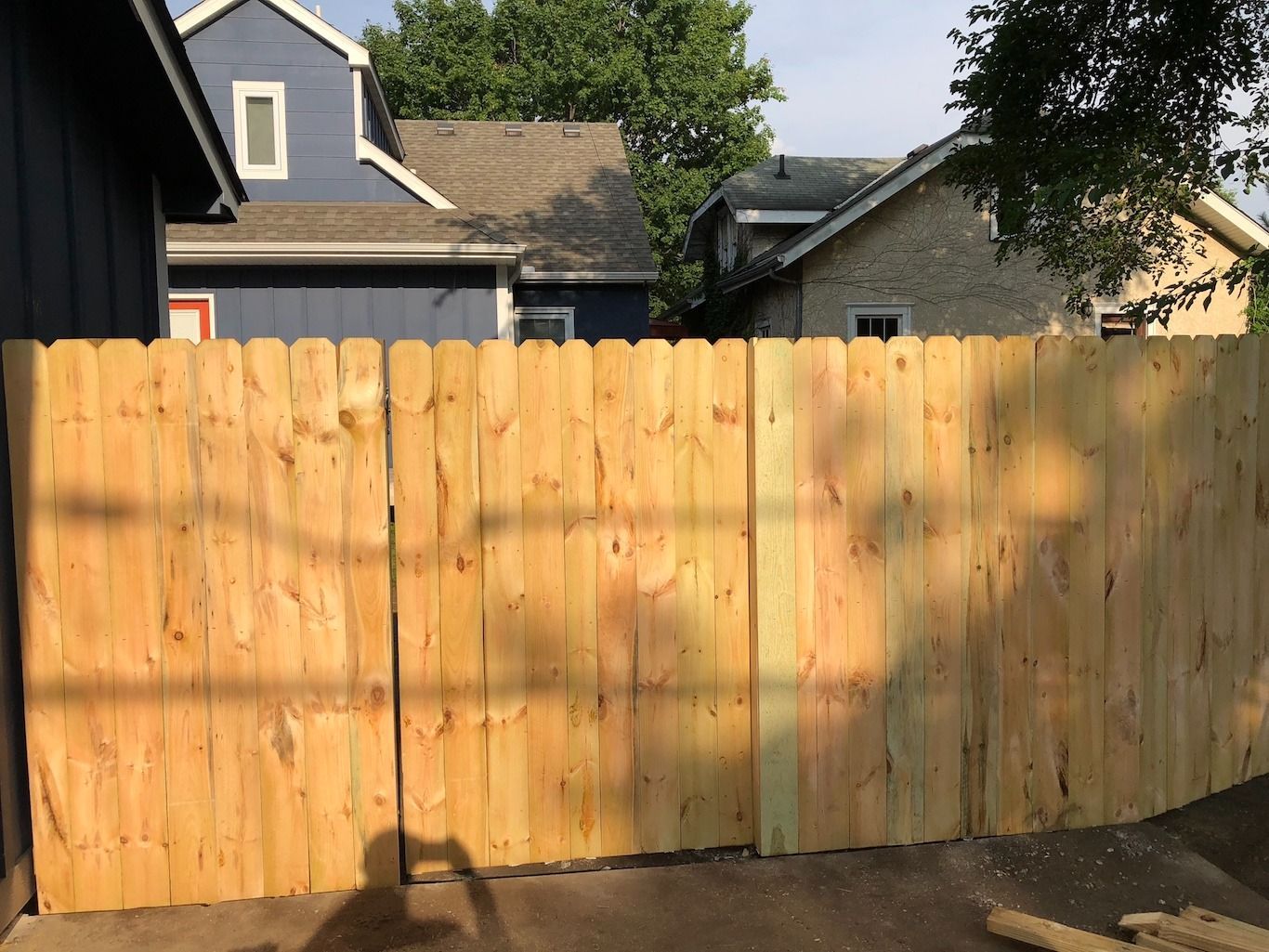 Wooden backyard fence with houses and trees visible behind it in daylight