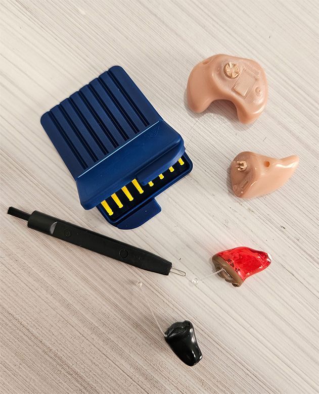 Blue hearing aid with black tool and four small ear molds on a light surface
