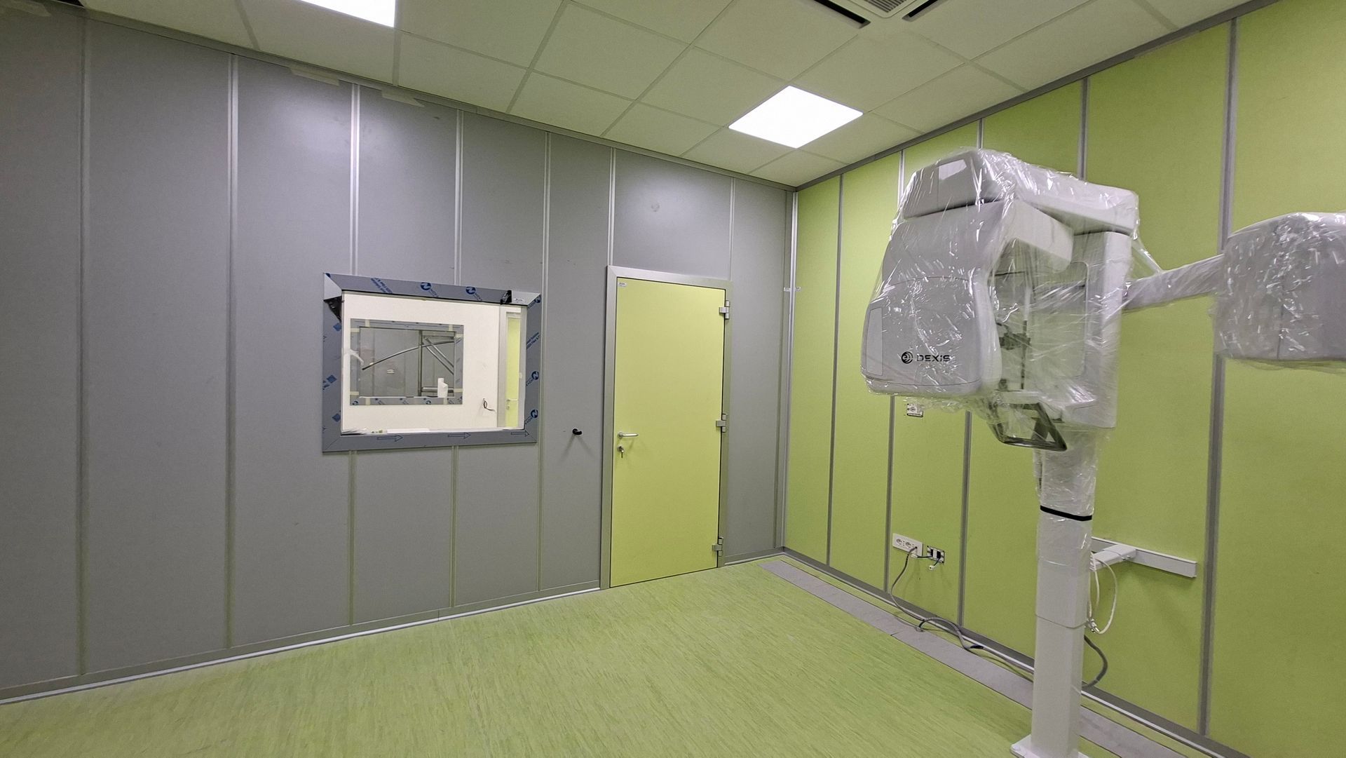 Grandi porte industriali bianche con un cartello di avvertimento sulle radiazioni in un corridoio; un operaio è in piedi sulla destra.