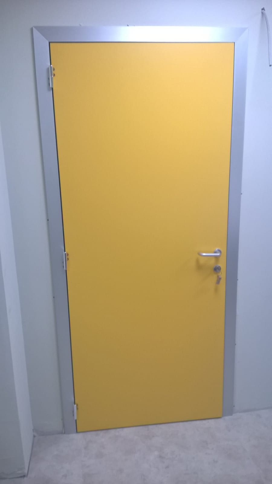 Porta industriale verde con cartello giallo di avvertimento sulle radiazioni e maniglia in metallo.