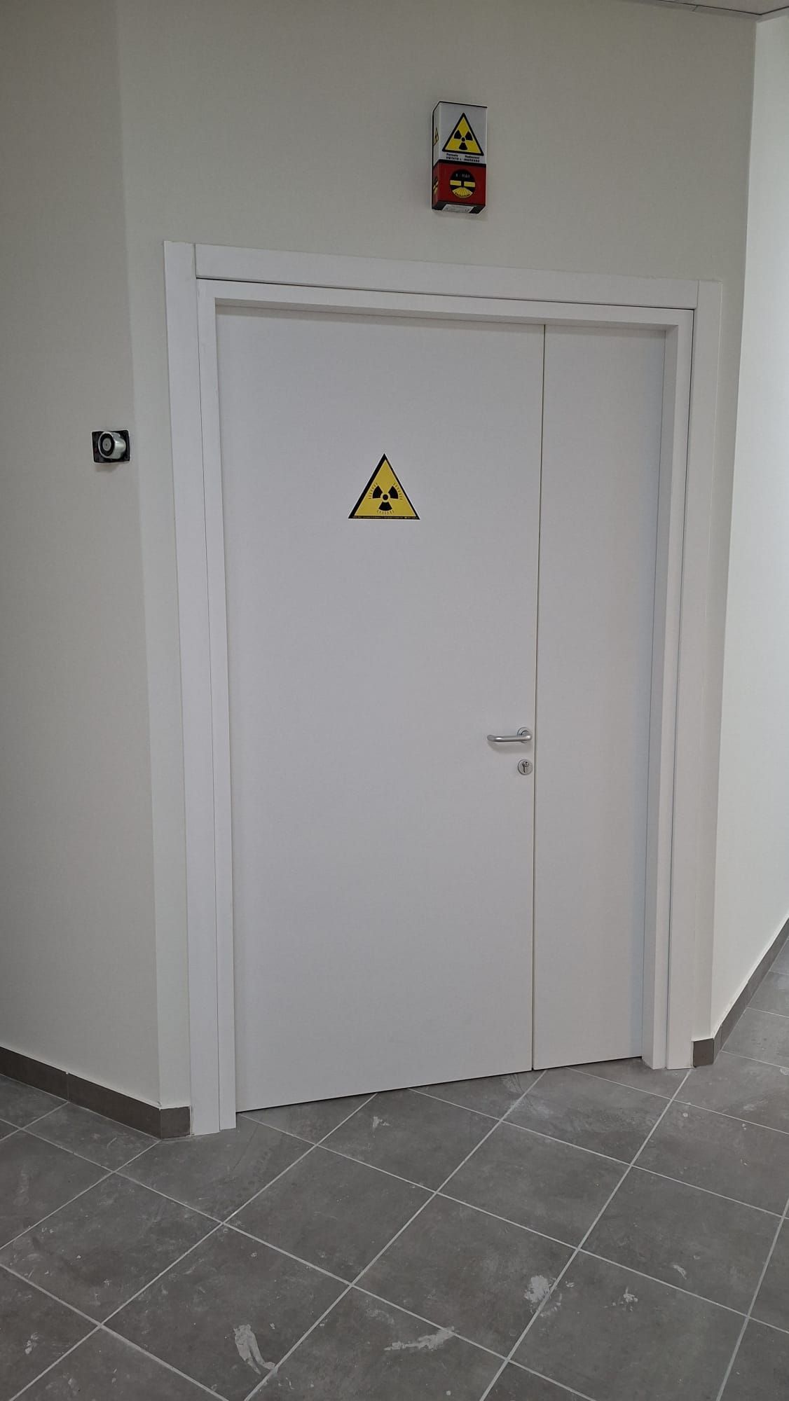 Porta industriale verde brillante con cartello di avvertimento in un corridoio grigio con pavimento verde