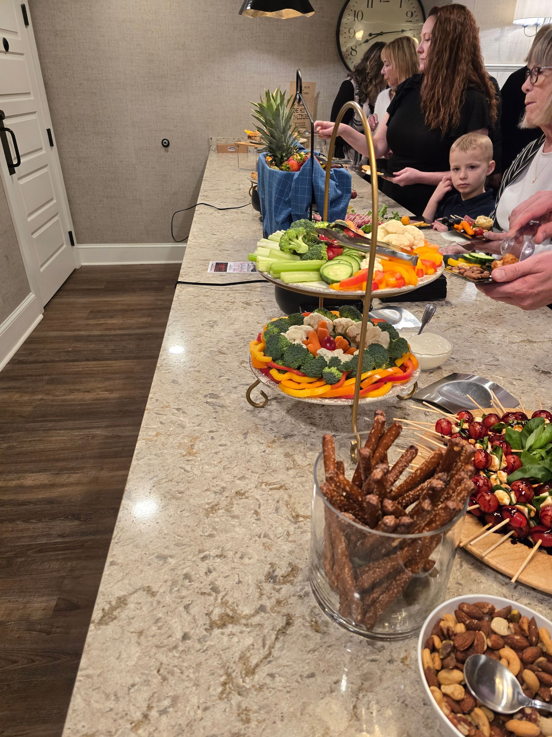 Buffet table with fruit, pastries, and appetizers while people serve themselves at a gathering