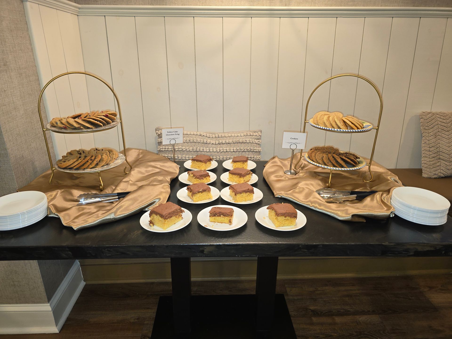 Dessert buffet with pastries and plates on a black table against a beige wall