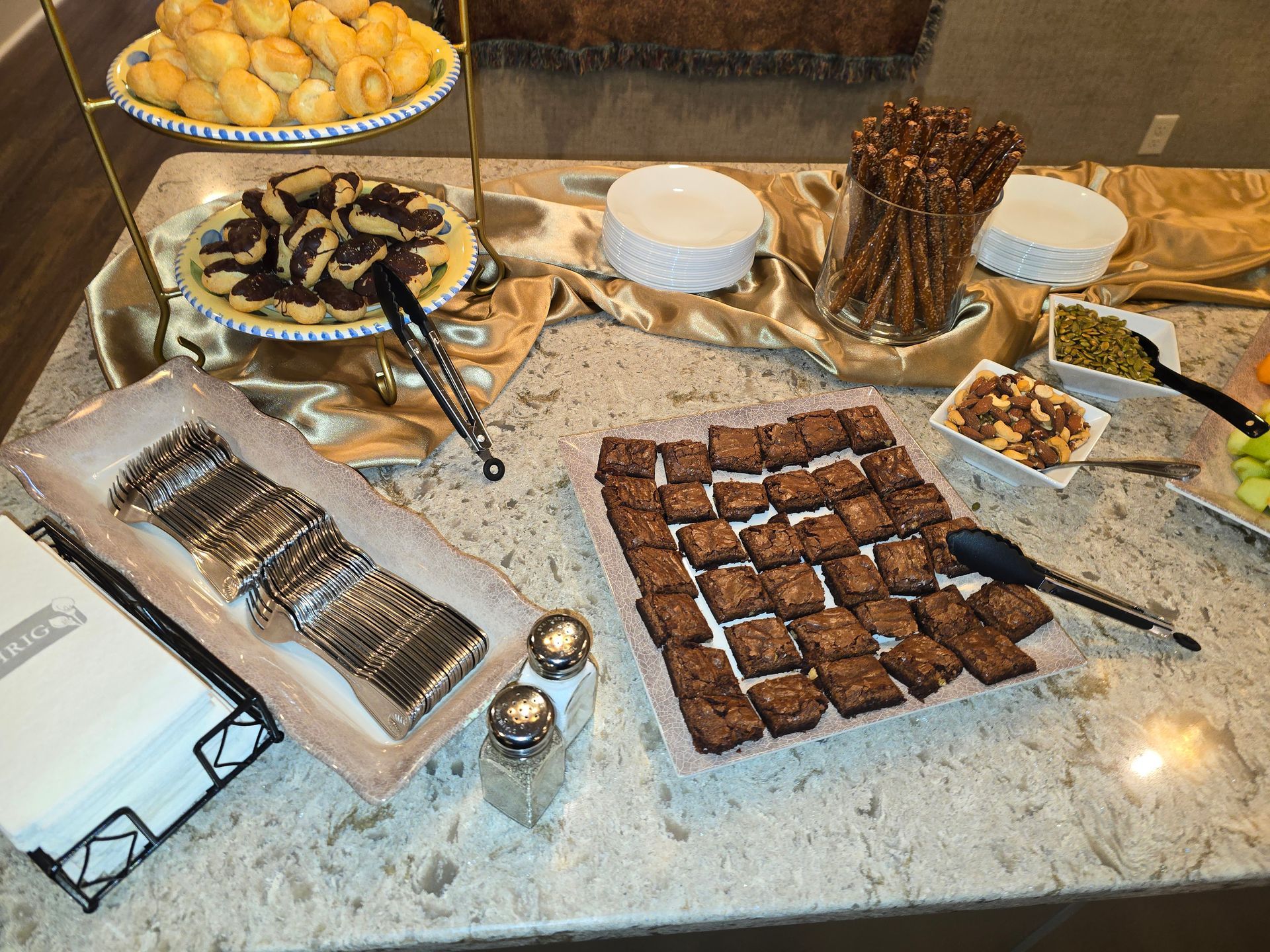 Dessert buffet on a marble counter with brownies, cookies, pastries, and serving tongs