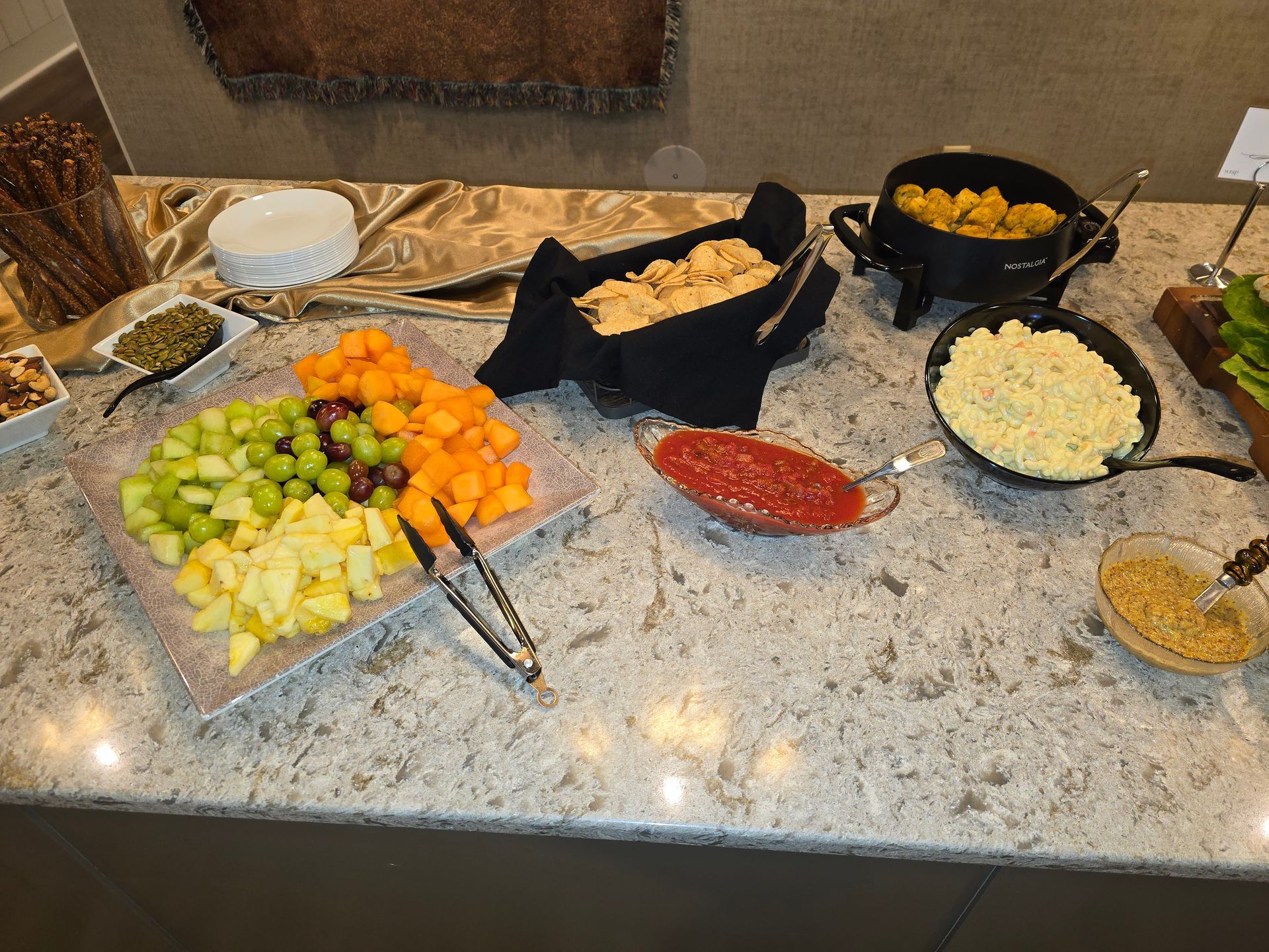 Buffet spread with fruit, dips, crackers, chips, and bowls on a granite counter
