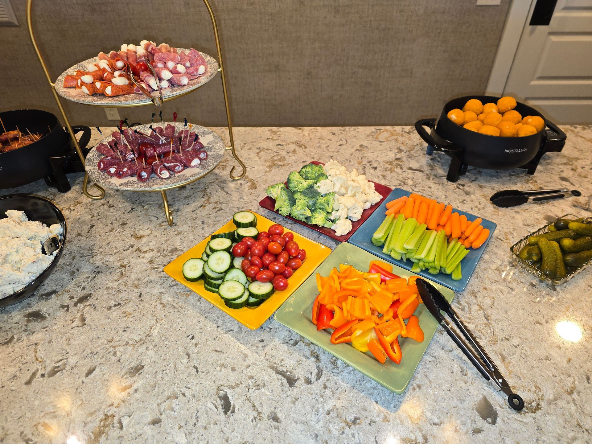 Buffet table with assorted sliced fruits and vegetables arranged on platters beside bowls of oranges and garlic cloves